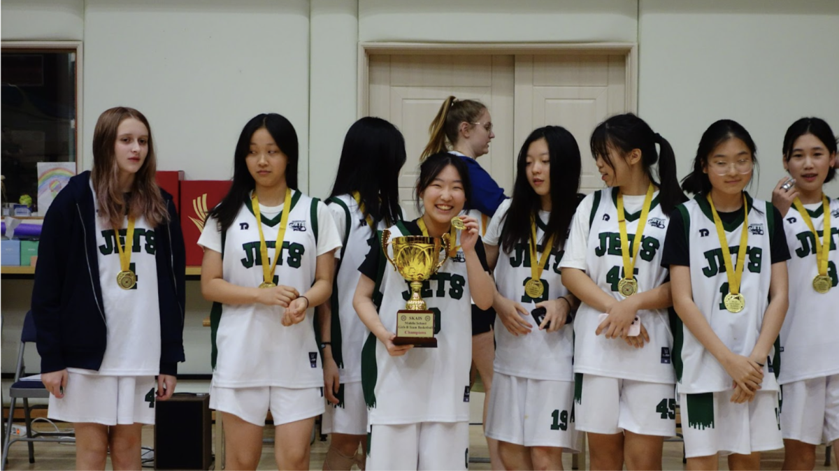 The junior varsity girls basketball team celebrates their championship victory, proudly displaying their first-place medals and hoisting the trophy after a series of hard-fought games.